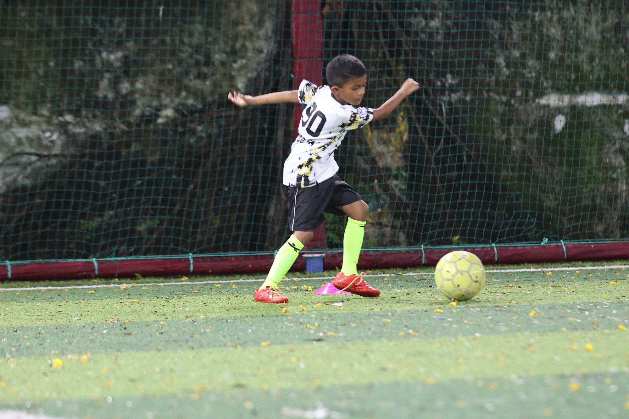 A player in a white kit dribbling through cones at night