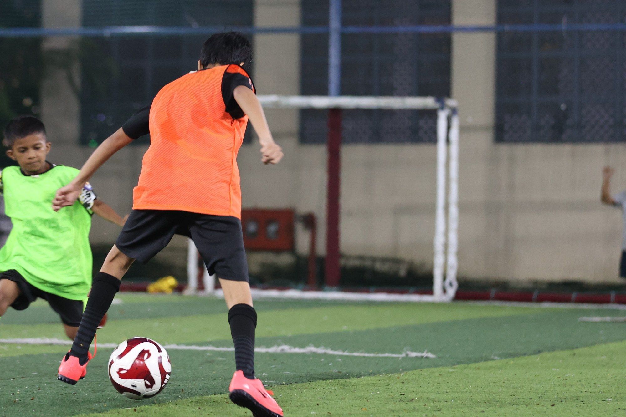 Two players in orange and green bibs battling for the ball