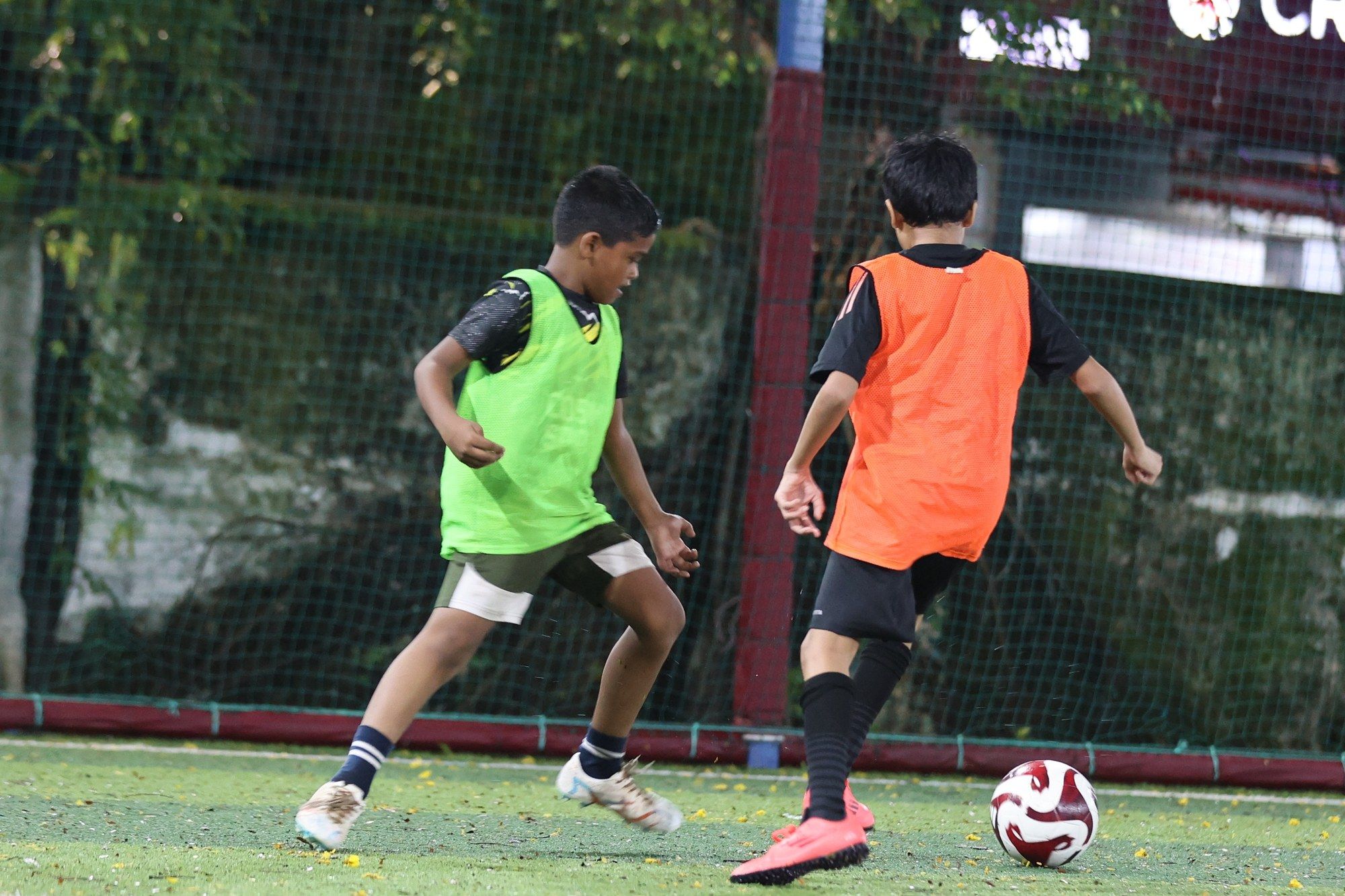A player in a green bib taking on a player in orange