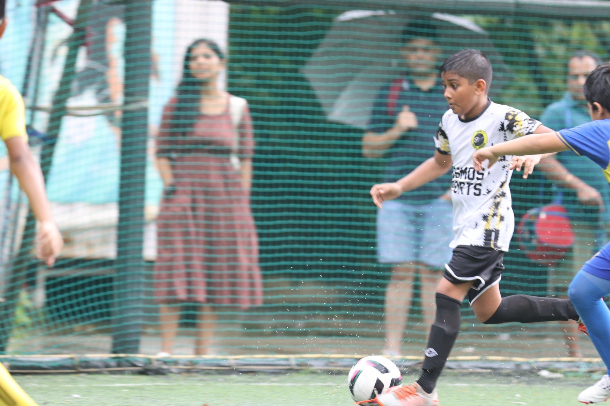 A player running with the ball as parents watch with umbrellas