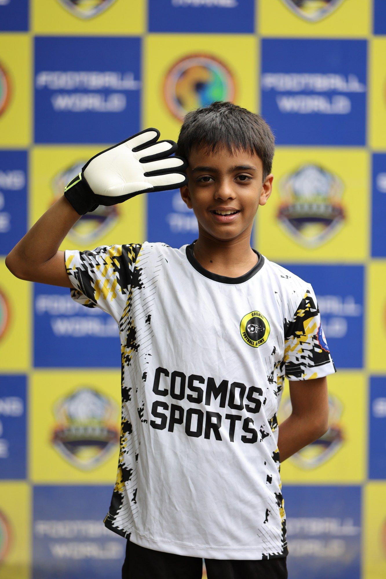 A goalkeeper in white raising a gloved hand for the camera